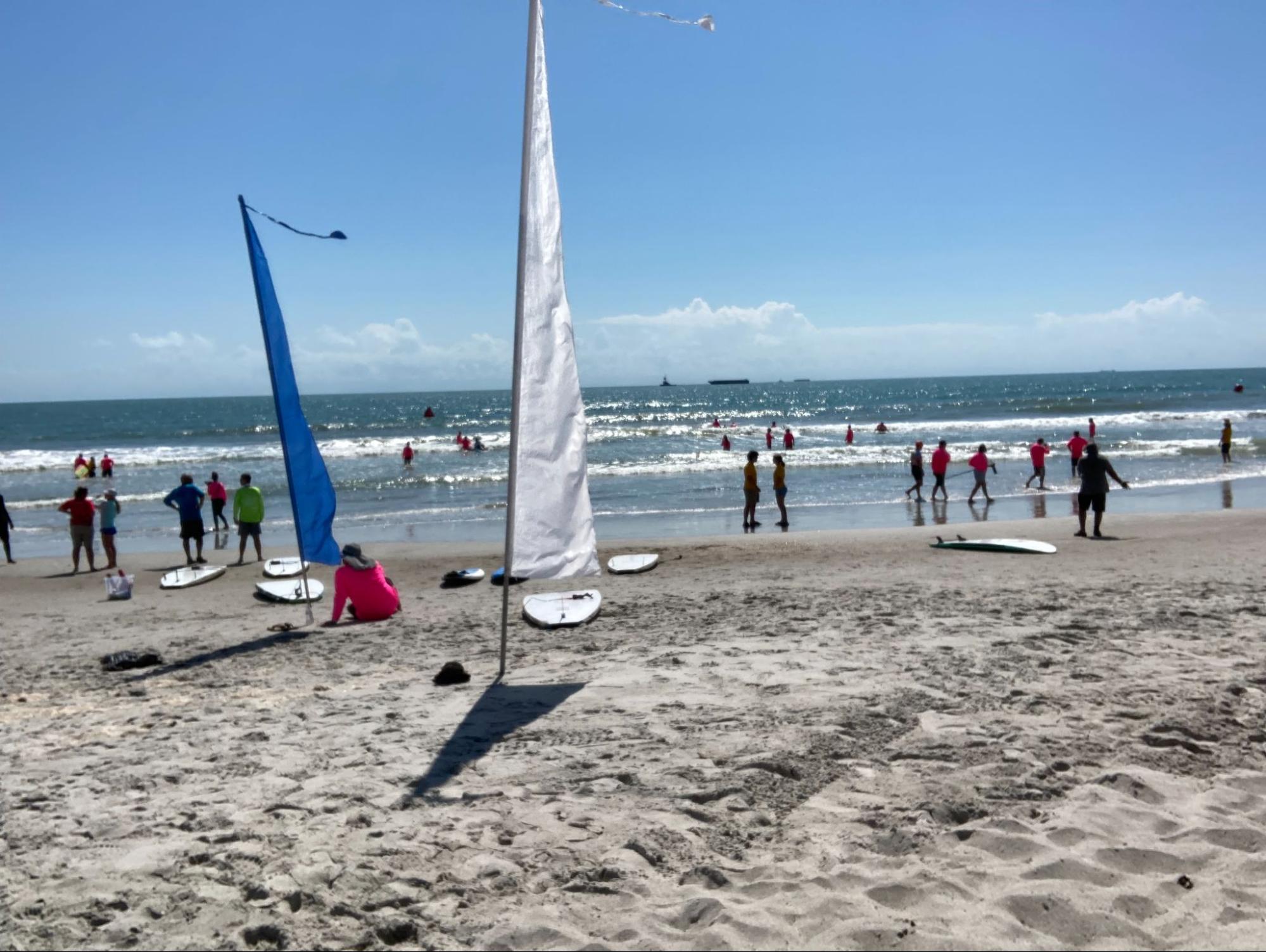 Picture of surf competition. Surf Athletes are catching waves as supporters watch from the beach. 